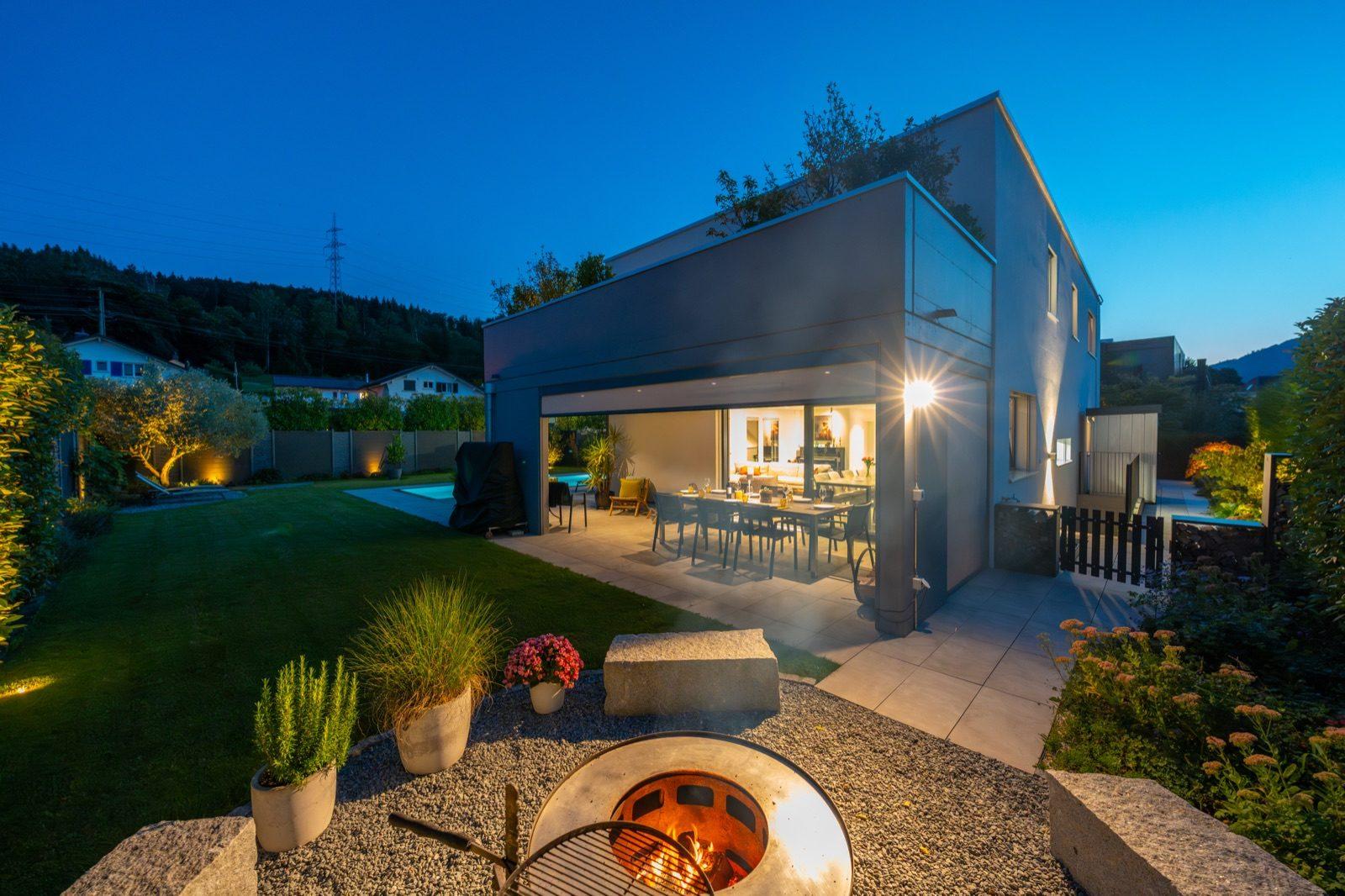Kubisches Wohnhaus mit Feuerschale und Pool zur blauen Stunde